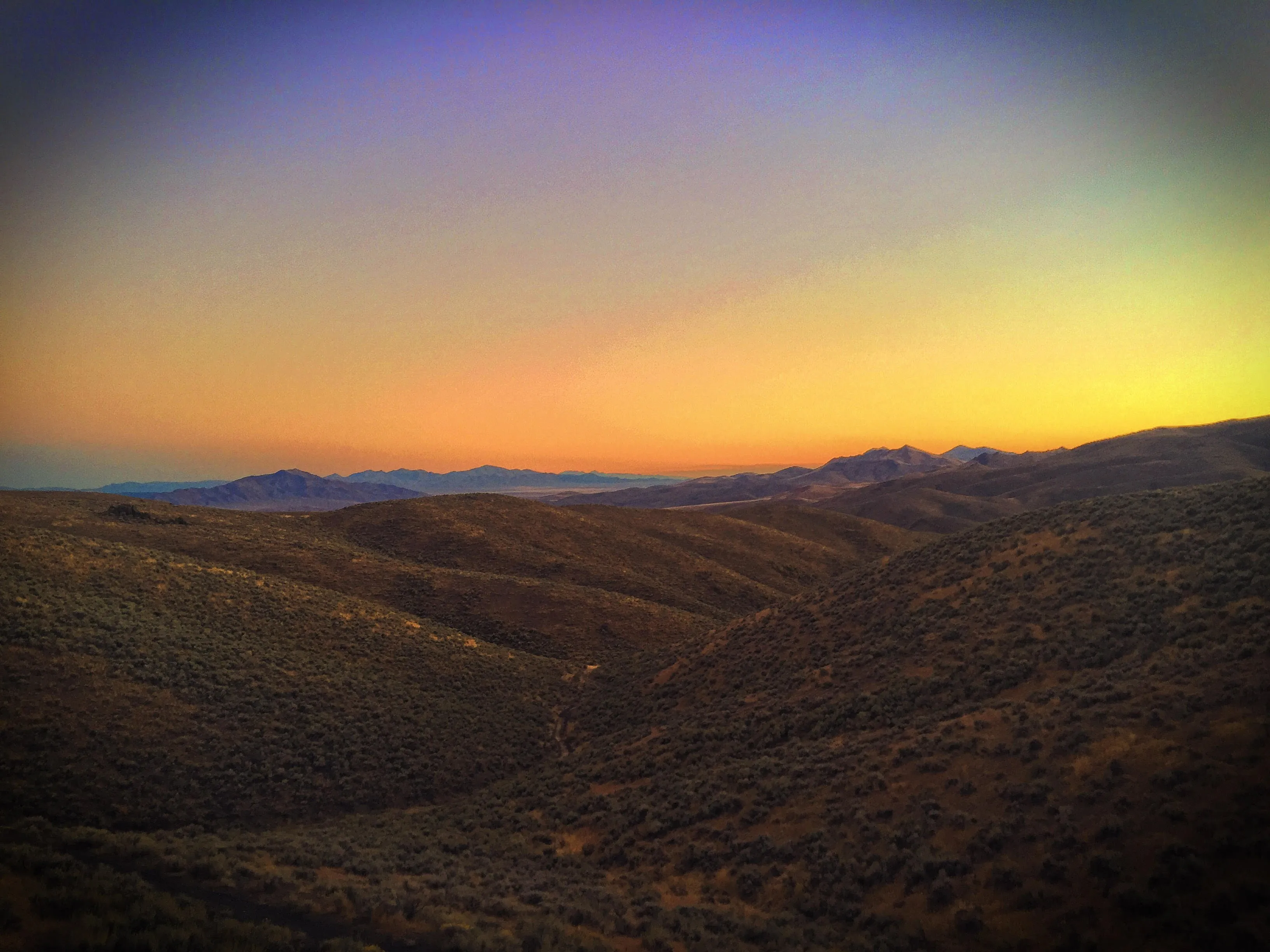 A wide band of colour across the sky at sunset over desert hills