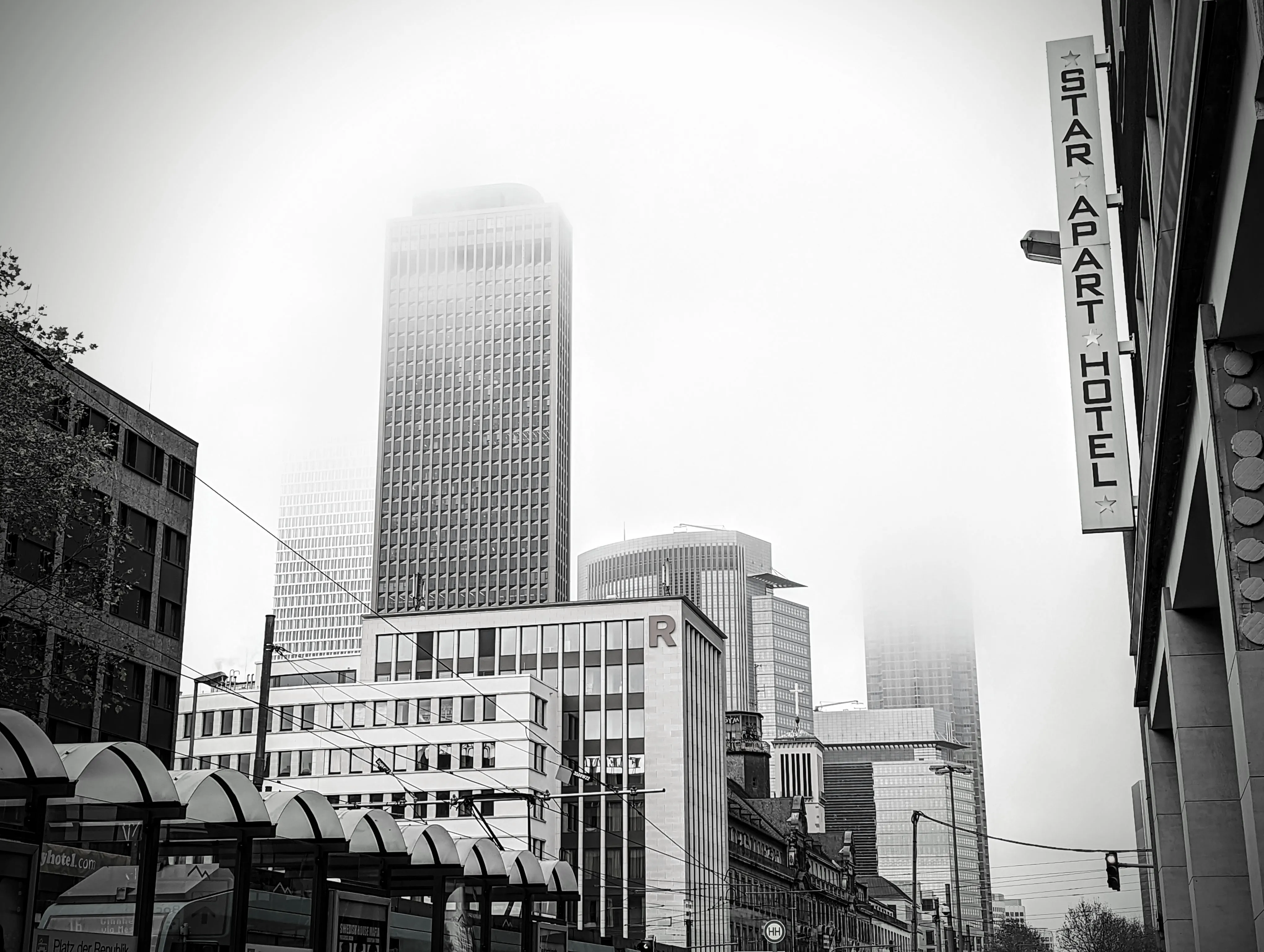 Black and white shot of a high-rise tower disappearing into fog, a hotel sign in the foreground