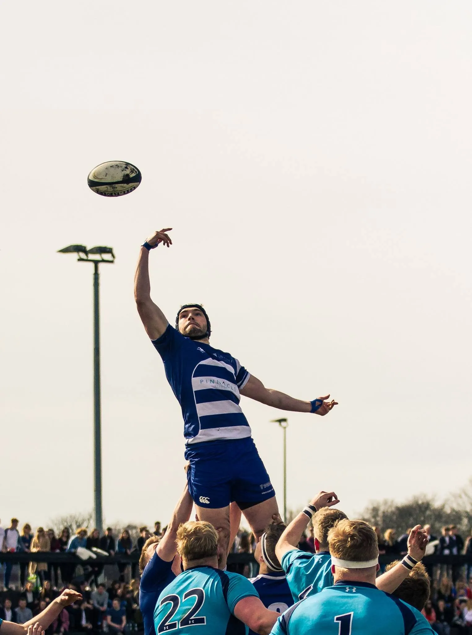 A rugby player fully airborne catching a lineout throw against a flat white sky