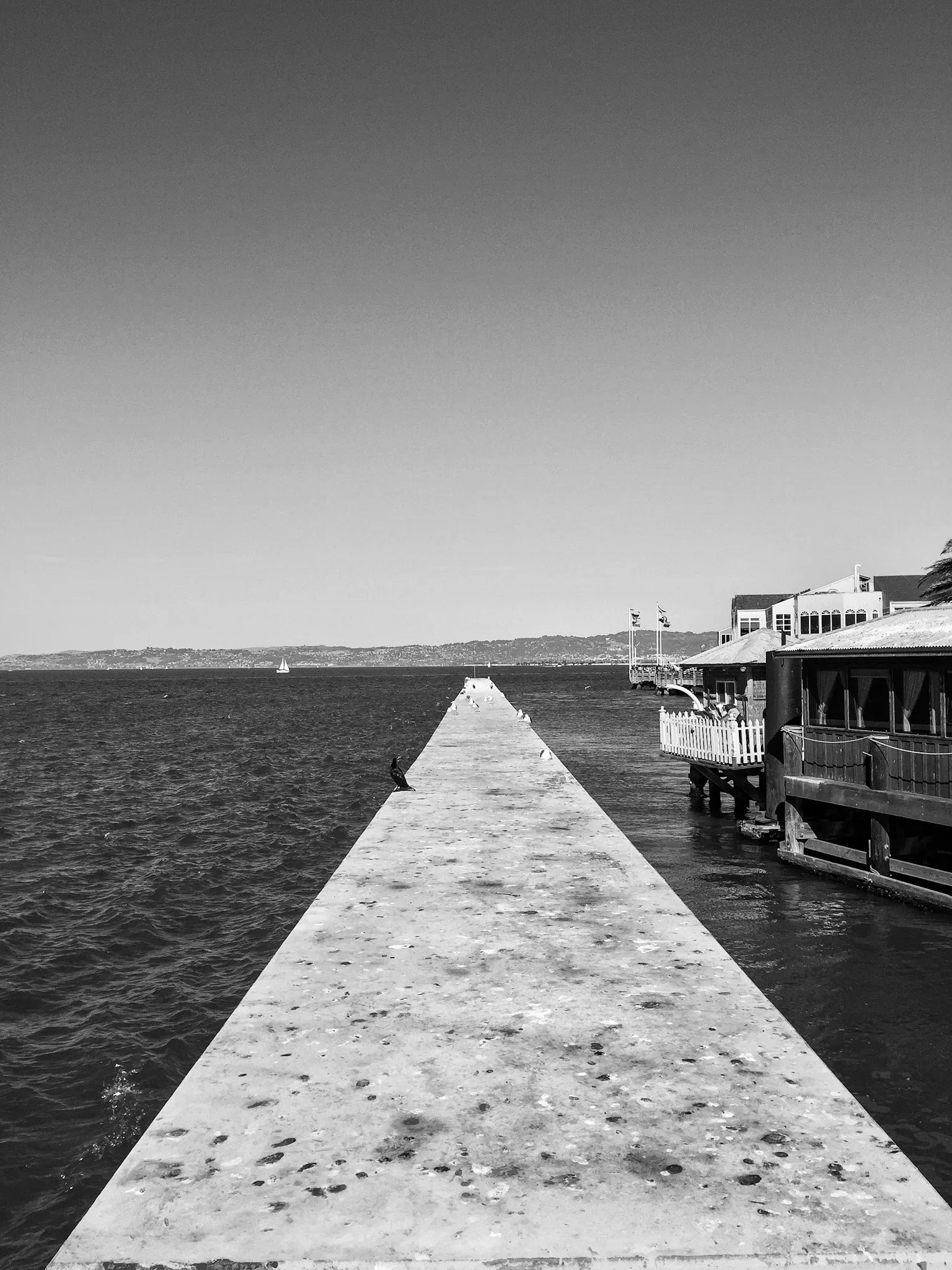 Black and white photo of a pier stretching to a vanishing point on the water