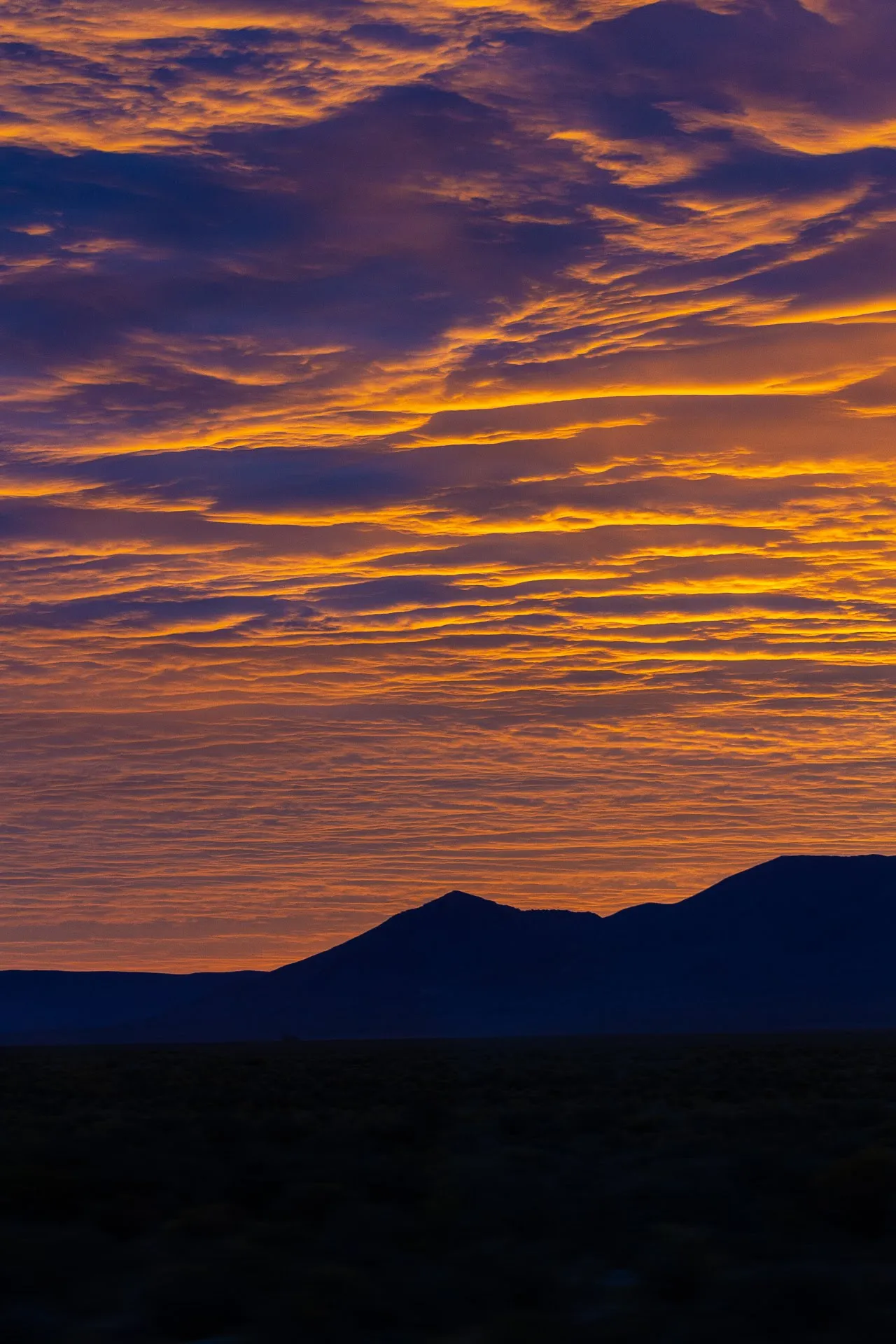 Streaky orange and gold sunset clouds over a dark silhouetted mountain ridge