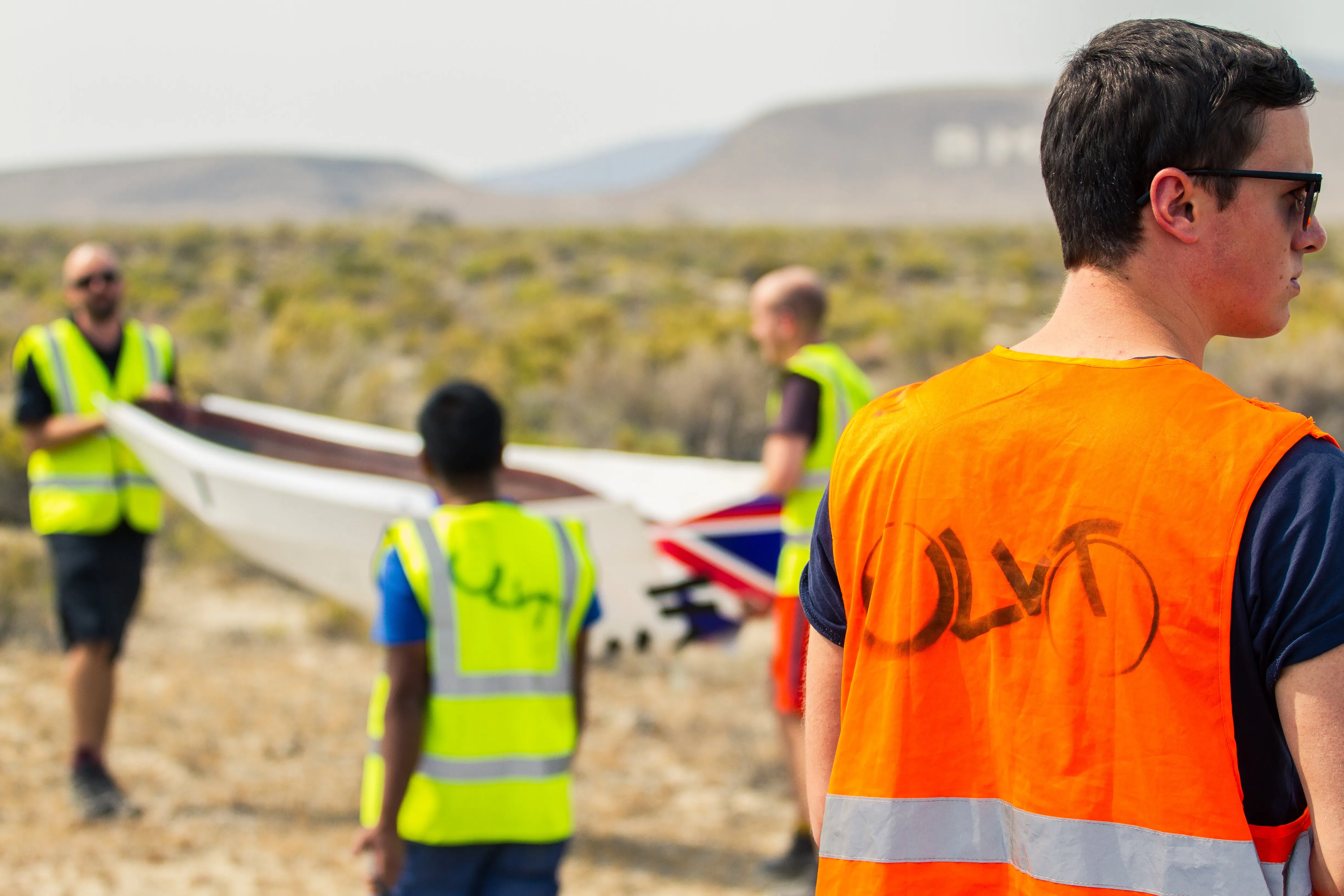 Team members in hi-vis carrying a fairing across the desert