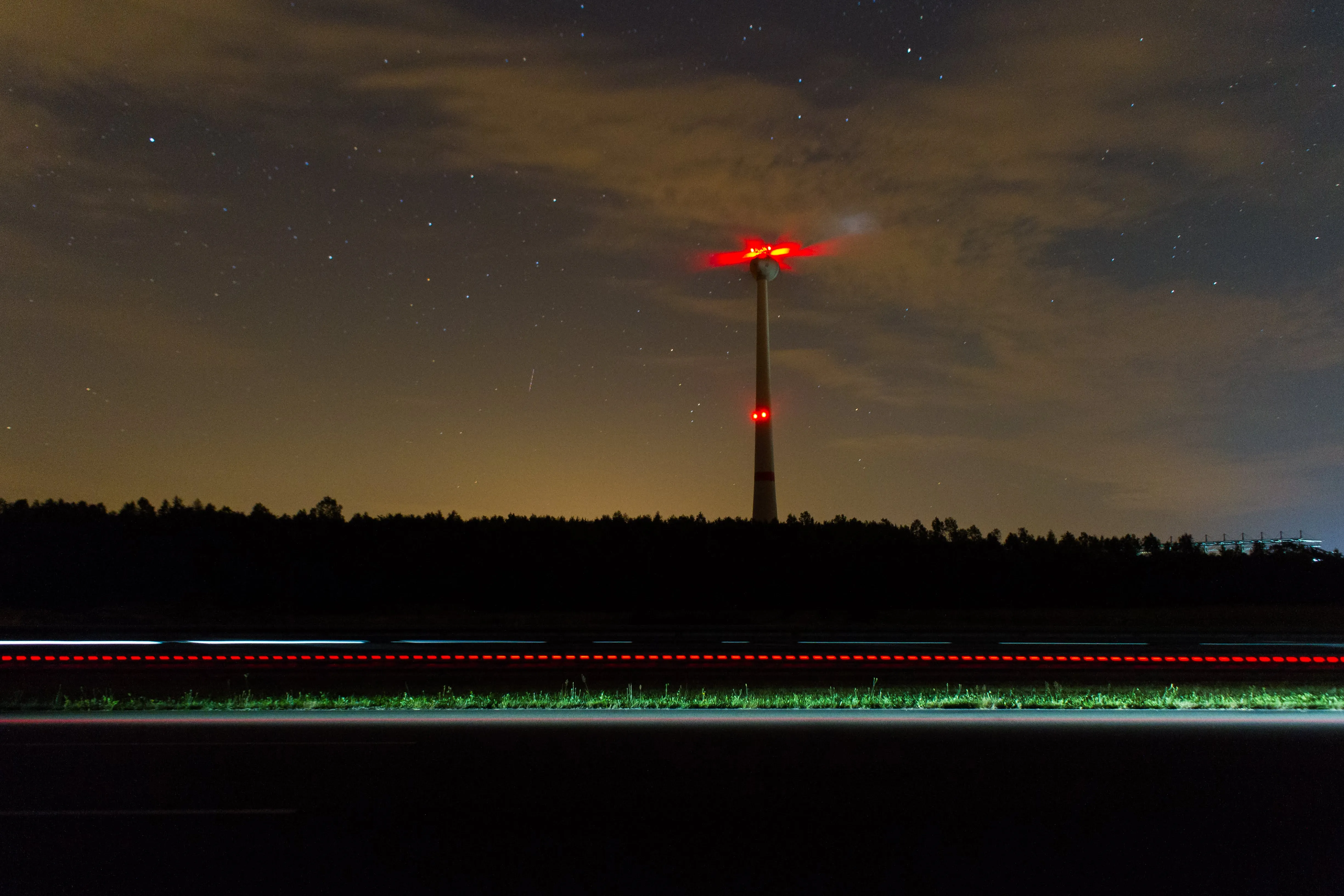 Long exposure at night showing a wind turbine and a streak of light from a passing vehicle